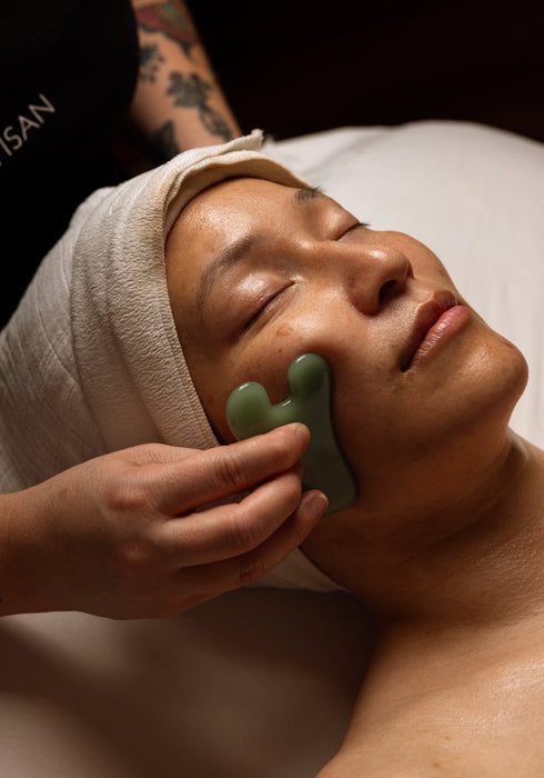 Person receiving a facial treatment with a green tool, wearing a towel on their head.