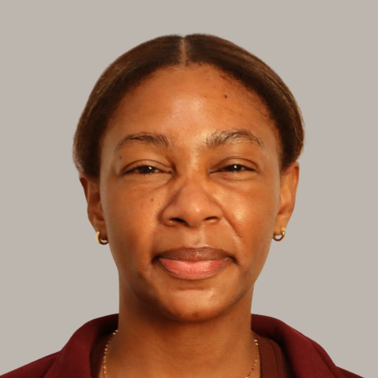 A close-up portrait of a woman with dark brown hair pulled back, wearing small gold hoop earrings and a burgundy top, set against a solid gray background.