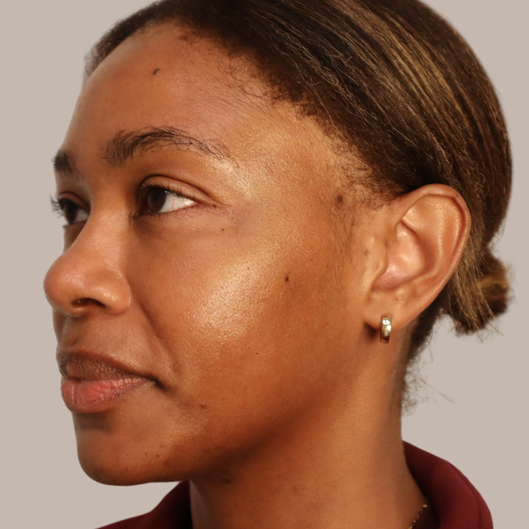 Close-up side profile of a woman wearing a small silver stud earring with a clear gemstone, against a plain light gray background.