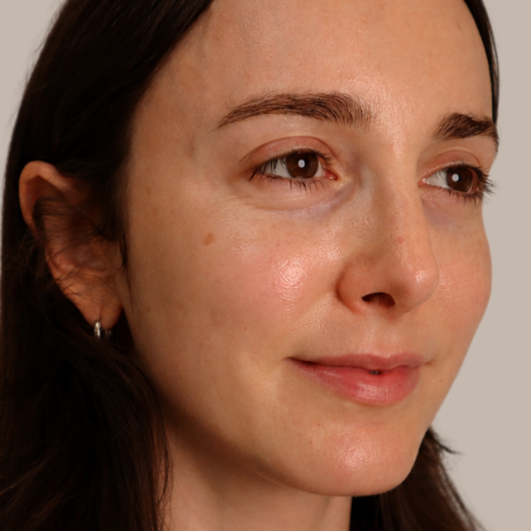 A close-up portrait of a woman with dark hair, wearing a small silver hoop earring, set against a plain light gray background.
