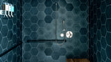 A modern walk-in shower stall with dark blue hexagonal wall tiles, a matching textured floor, a wooden bench mounted on the right wall, and a chrome shower fixture.
