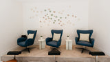 A staged interior room with three blue lounge chairs arranged on a raised platform, each with a cream pillow. Two small white side tables sit between the chairs, and a decorative cluster of circular wall decals is mounted on the white wall above.