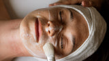 Person receiving a facial treatment with a brush on a white background