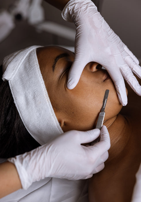 Person receiving a facial treatment with gloved hands using a tool.