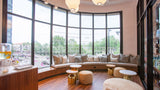 A modern spa-style interior with a curved upholstered bench, round ottomans, small round tables, large black-framed windows, and pendant lights. No person or animal is present, and the scene appears to be a real environment rather than a clean isolated product shot.