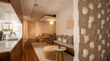 A modern interior space with a beige upholstered sofa, round ottoman, small round coffee table, wood flooring, and a decorative geometric wall panel on the right.