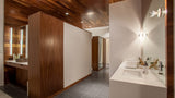 A modern bathroom interior with dark wood cabinetry, a white vanity, gray floor tiles, and a large wall mirror.