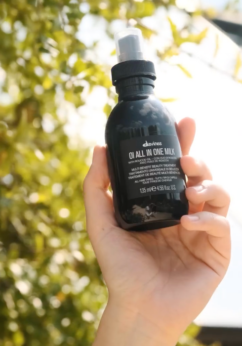 Hand holding a black bottle labeled 'All in One Wax' against a blurred green outdoor background