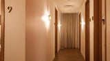 A warm, softly lit hotel hallway with cream-colored walls, wooden doors, a wood floor, wall-mounted sconces, and a beige curtain at the end of the corridor.