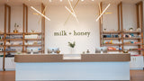 Modern interior of a store named 'milk + honey' with wooden shelves and a reception desk.