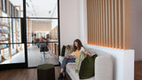 Woman reading a book on a couch in a modern interior setting with large windows.