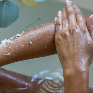 Person scrubbing their arm with a scrubber, with water droplets visible.