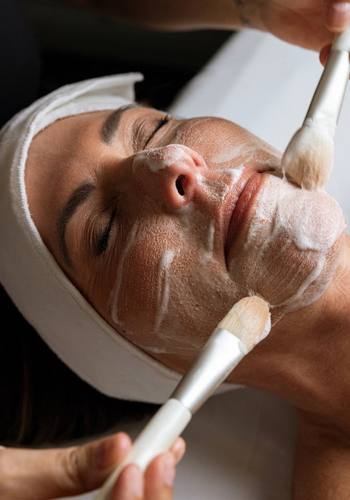 Person receiving a facial treatment with a white mask on their face.