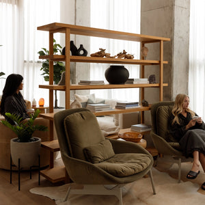 Two women in a modern living room with a wooden bookshelf and comfortable chairs.