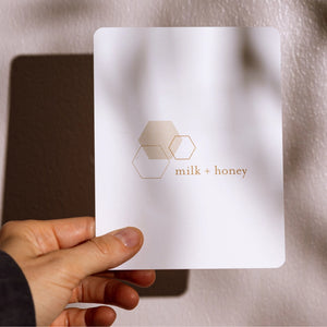 Hand holding a 'milk + honey' sheet mask against a neutral background