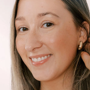 Woman adjusting an earring with a plain background