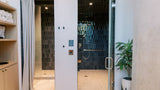 A modern indoor spa or shower facility with two glass-walled shower areas. One side has a light gray curtain, and the other has a glass door with a metal handle.