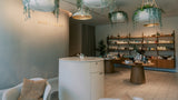 A modern spa or beauty retail interior with a round white reception counter, hanging planters, shelving filled with products, and neutral-toned seating. The wall displays the text 'milk + honey'.