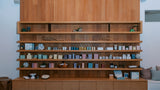 A large built-in wooden shelving unit with multiple tiers and a lower cabinet, displaying many small boxes, jars, and decorative objects in a home interior.