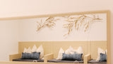 A minimalist interior scene showing a light wood bench with white and blue-gray pillows against a cream wall, with a large rectangular mirror above reflecting the scene and gold-toned dried botanical branches mounted on the wall.