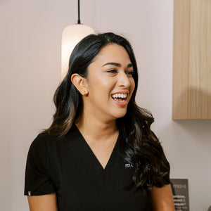 med spa provider wearing a black scrubs with the milk and honey logo, standing in a med spa treatment room.