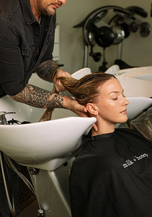 Person getting a hair wash at a salon with a stylist and sink in the background.