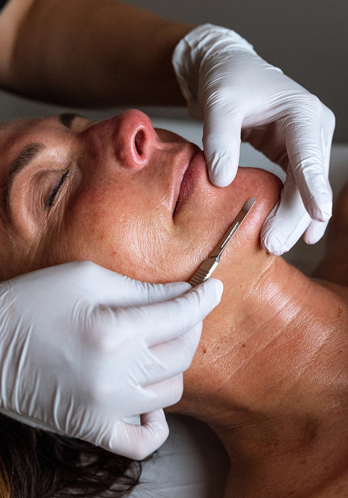 Person receiving a facial treatment with gloved hands using a tool on a neutral background